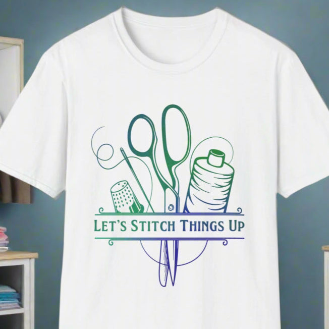 White t-shirt with a graphic that includes a pair of scissors, a spool of thread, and the text 'LET'S STITCH THINGS UP', displayed in a room with sewing-related items in the background.