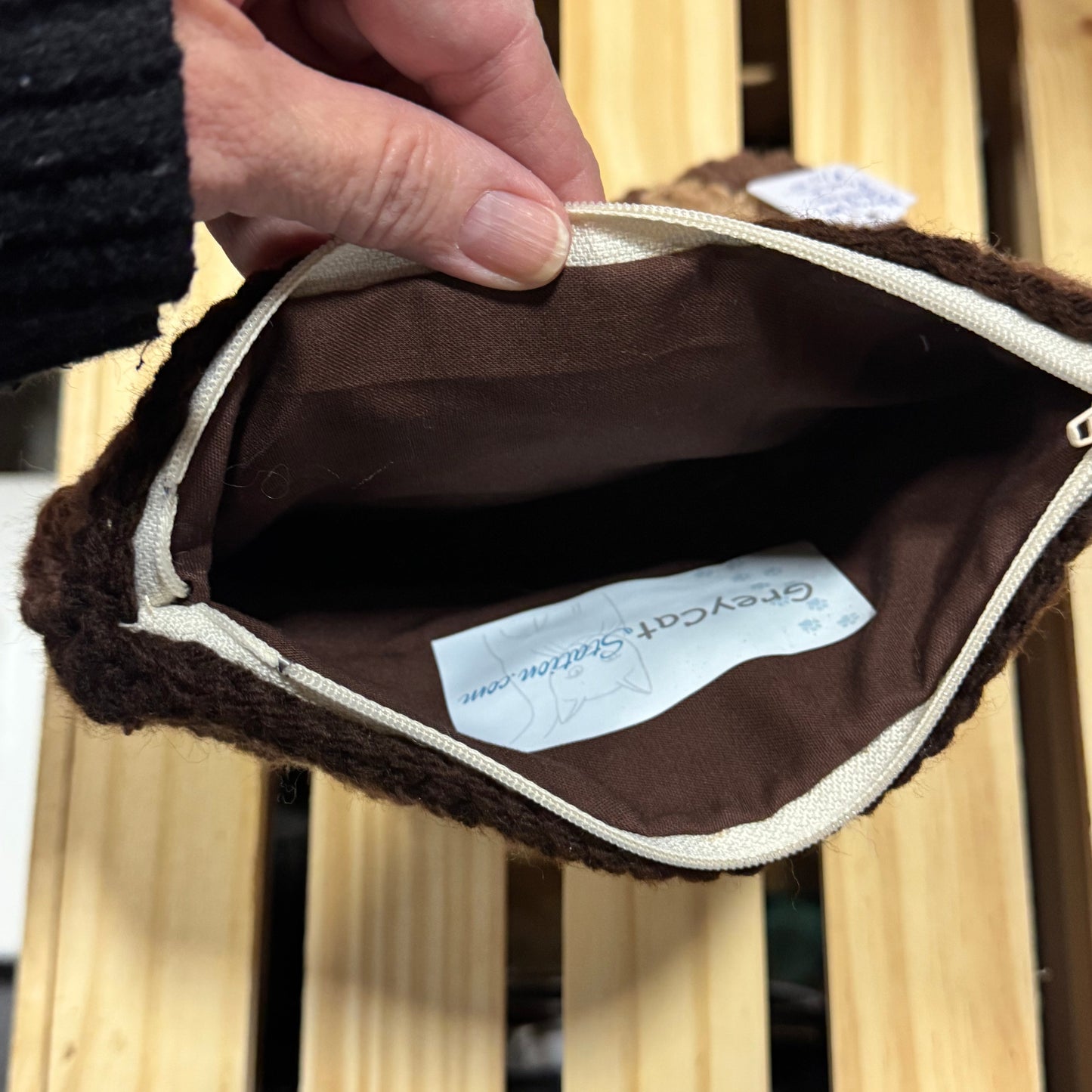 Brown pouch with a visible brand label held by a hand against a wooden background