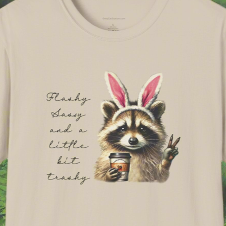 A beige t-shirt with a graphic print of a raccoon wearing bunny ears and text that reads 'Flashy Sassy and a little bit trashy'. 