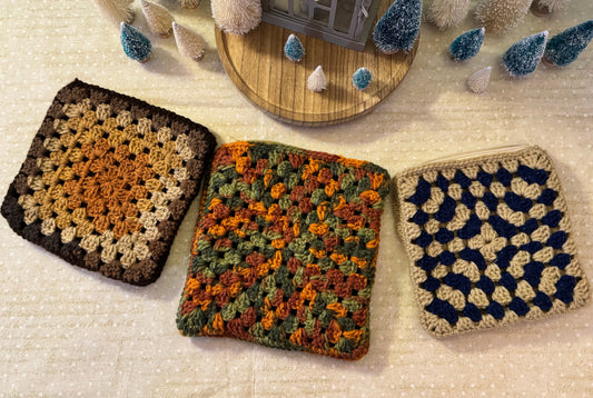 A collection of crochet pouches with zipper closures, displayed on a table. They come in multiple colors including brown, multicolored, and blue.